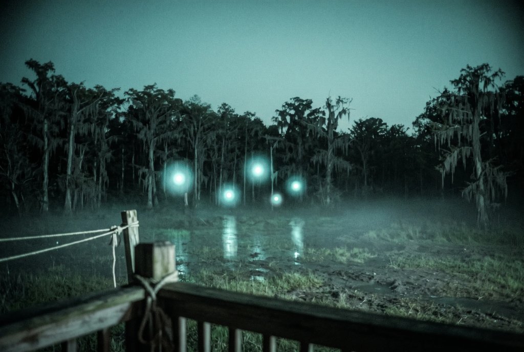 five pale lights hovering in front of a swamp treeline, photographed from a camp porch